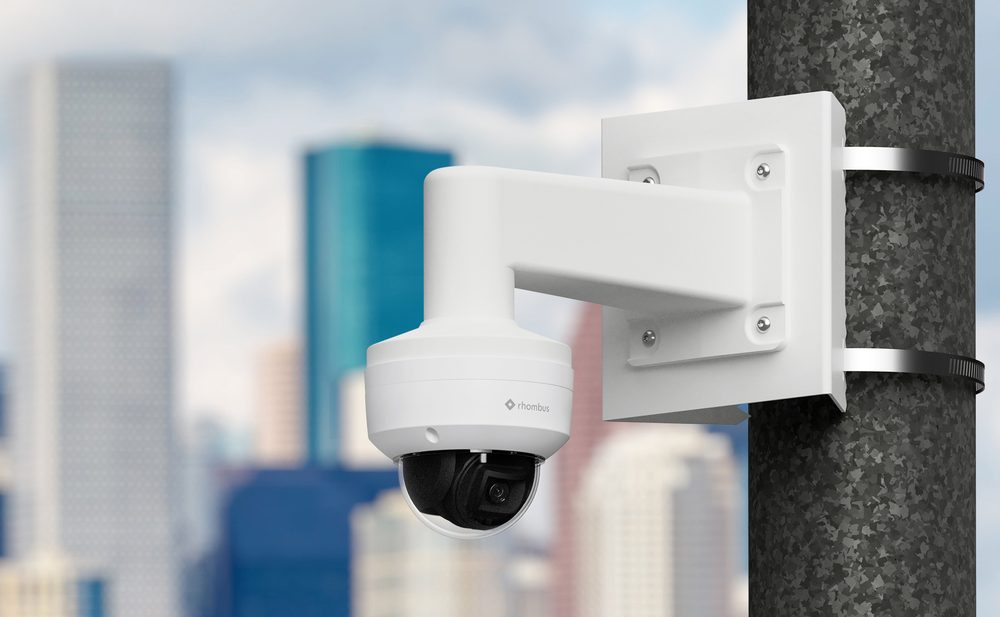 Rhombus R200 outdoor dome camera mounted on a pole bracket with a city skyline behind